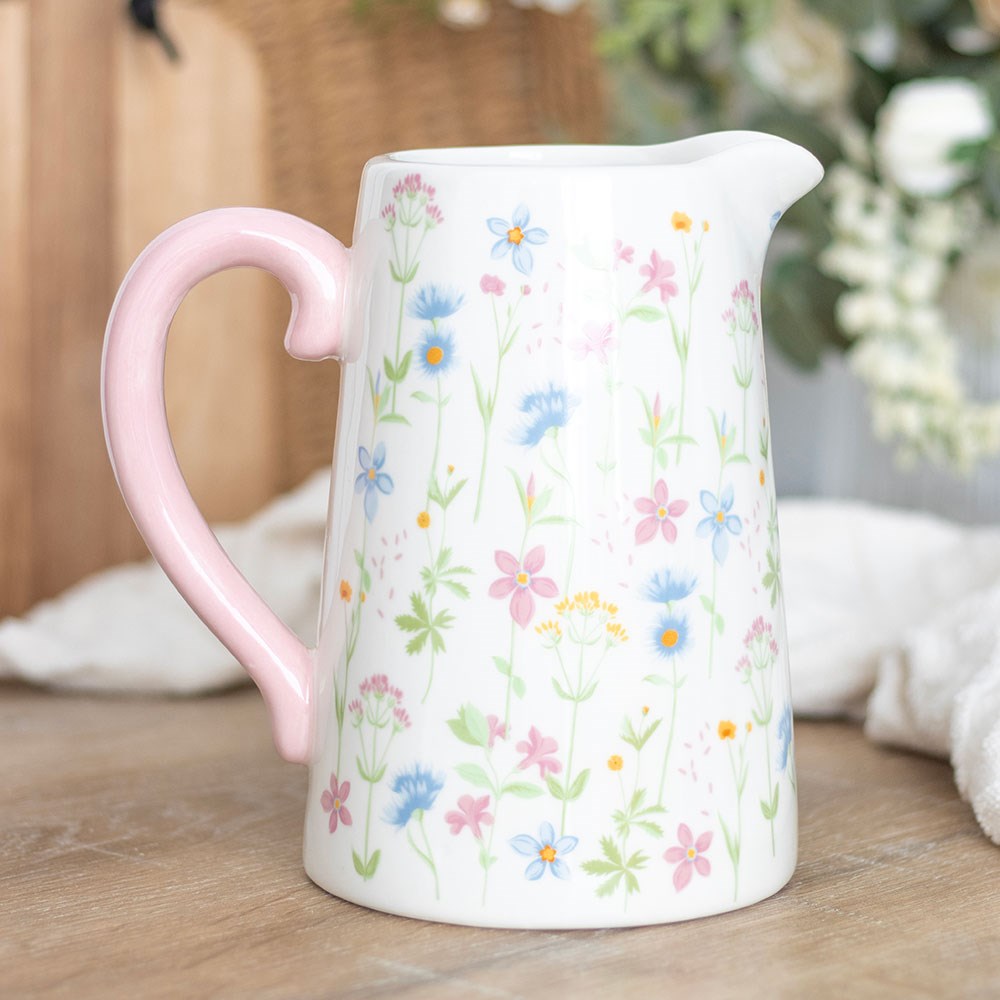 white ceramic jug shaped vase with floral design on and a pink handle.