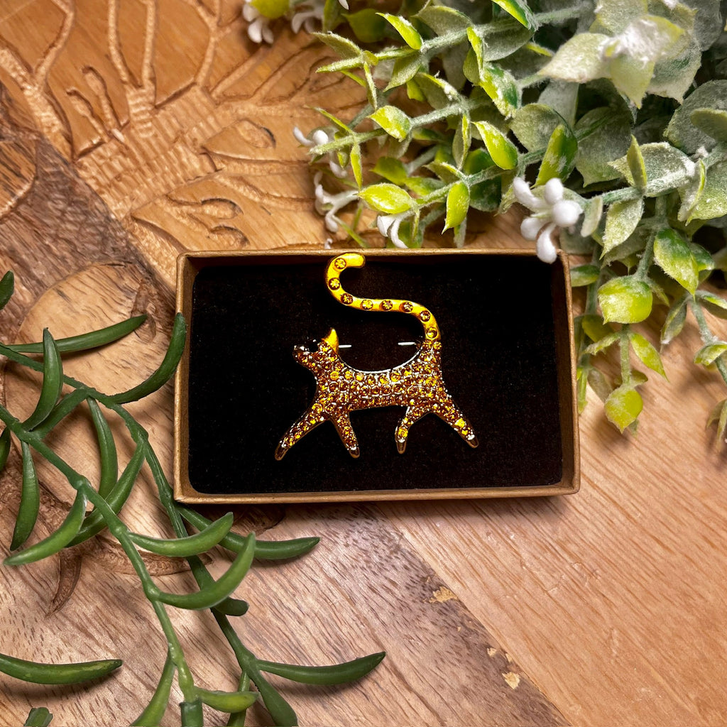 Walking orange cat brooch with orange rhinestones on its body and black rhinestones for eyes.