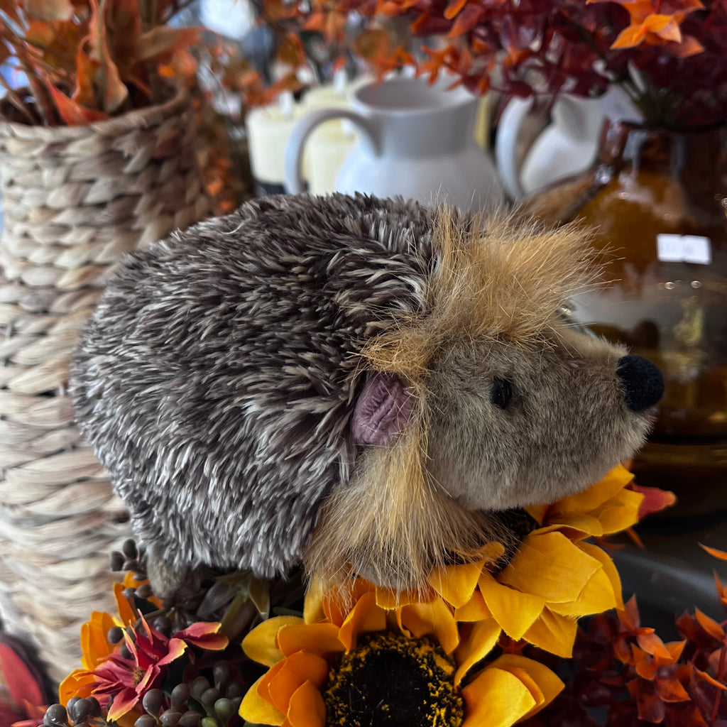 Plush hedgehog toy surrounded by sunflowers and autumn-themed decor