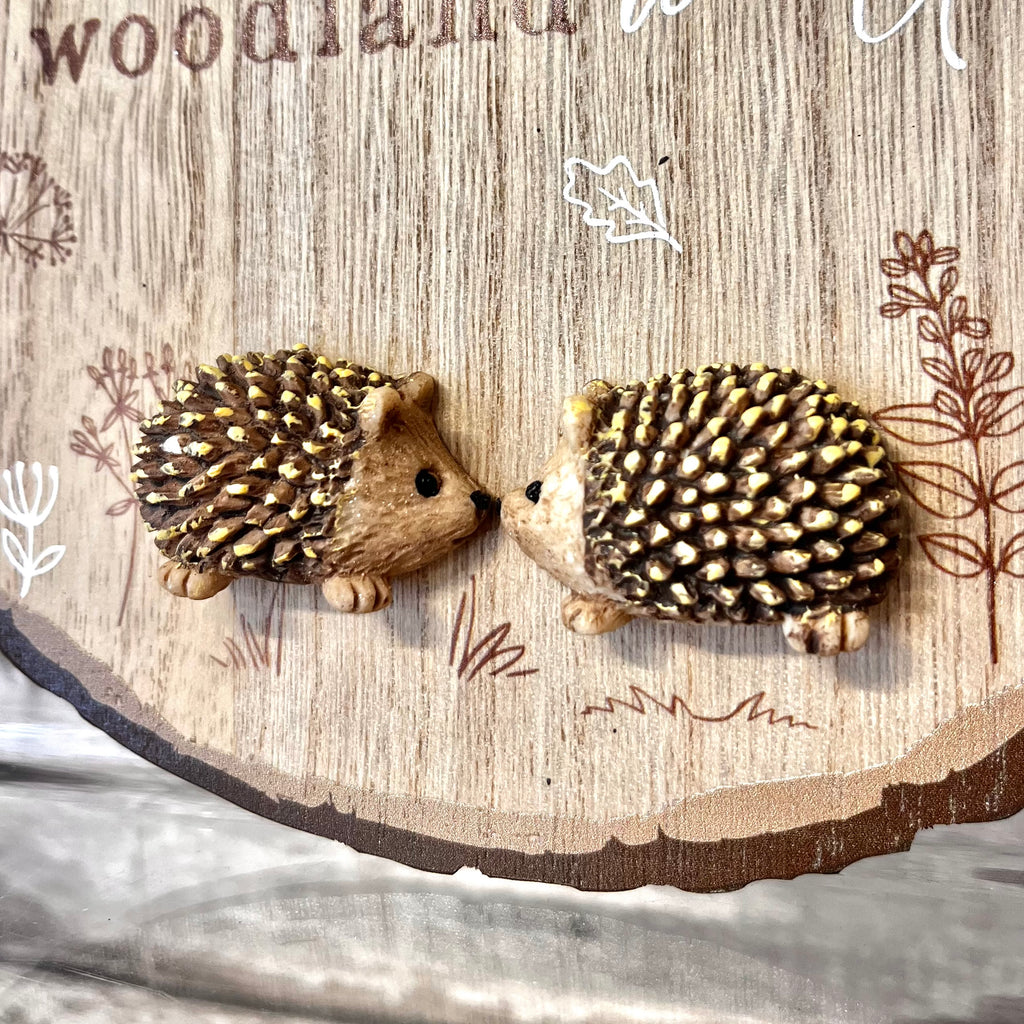 Two hedgehog earrings on a wooden background with 'Woodland' text.