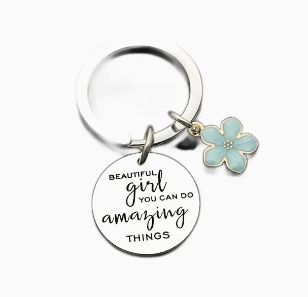 Silver keyring with round charm engraved with the test 'beautiful girl you can do amazing things' and features a blue glittery flower charm on gold hardware.